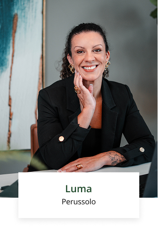 Uma mulher está sentada à mesa com a mão no queixo e sorrindo.