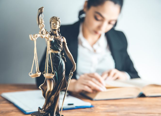 Uma estátua da justiça está sobre uma mesa ao lado de uma mulher lendo um livro.