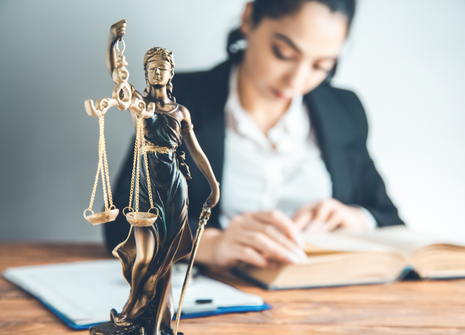 Uma estátua da justiça está sobre uma mesa ao lado de uma mulher lendo um livro.
