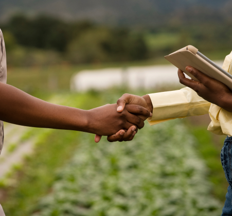 Duas pessoas apertando as mãos em um campo, uma delas segurando um tablet